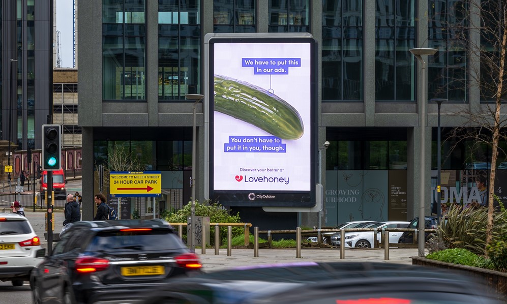 Image shows a billboard which contains a picture of a cucumber on a white background with the phrase "We have to put this in our ads. You don't have to put it in you though". Lovehoney is launching a new out-of-home campaign spotlighting the everyday household items people in the UK turn to for pleasure, in an effort to get around rules on advertising sex toys and encourage healthy conversation