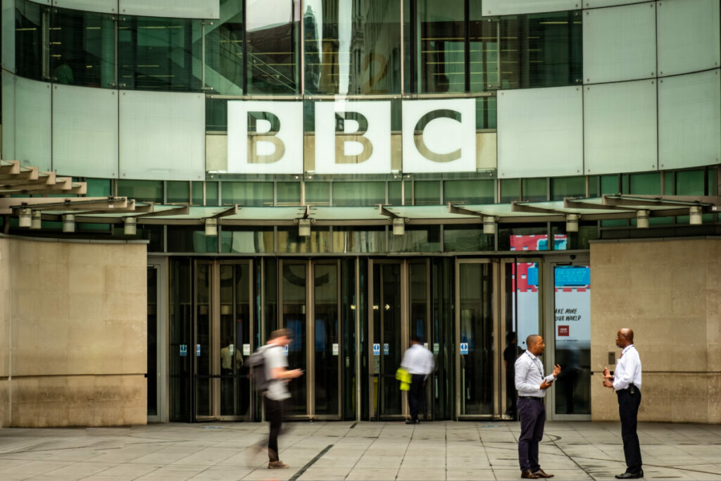 Workers stand outside the BBC building. A group of 20 media businesses have written to the government, expressing concern about the BBC's plans to introduce ads on audio content.
