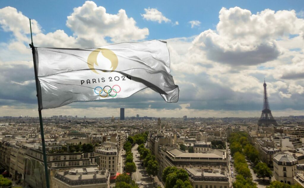 Olympic flag flies above a cloudy Paris. Badvertising finds that sponsorship deals between four giants and the Olympics amount to the same amount of emissions as eight coal plants.