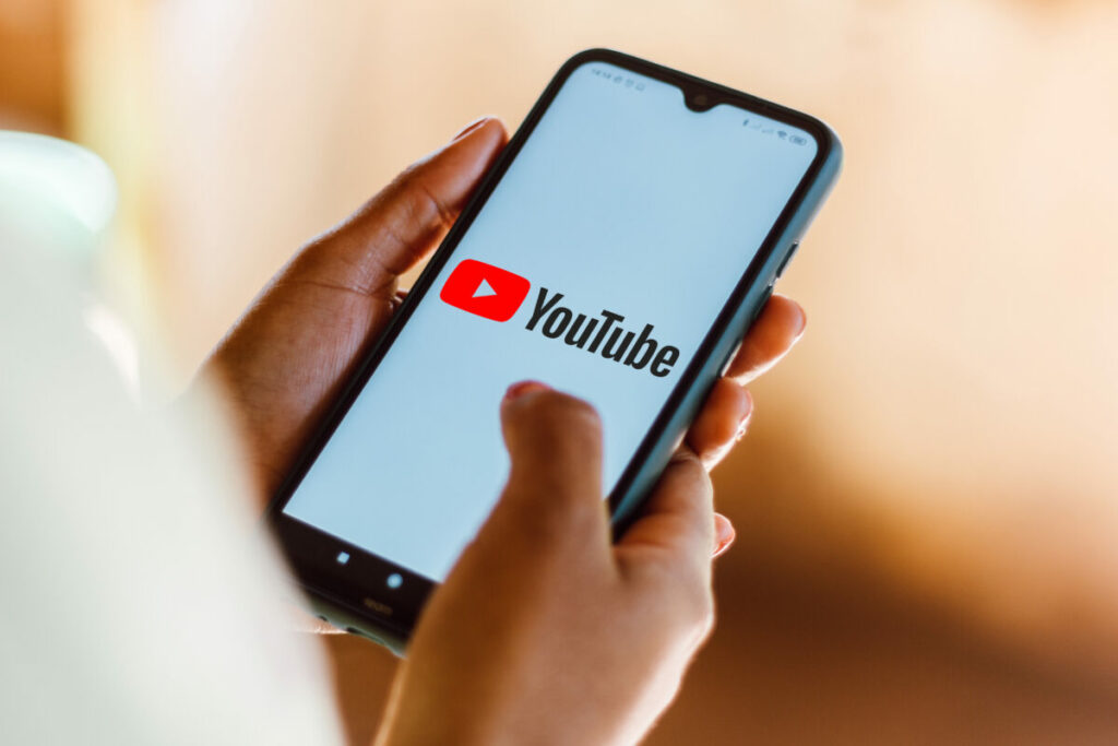 A person scrolls on their phone with Youtube in front of them. Youtube took to social media to highlight that the platform is serving them with blank ads or black screens before a video if they use an ad blocker.