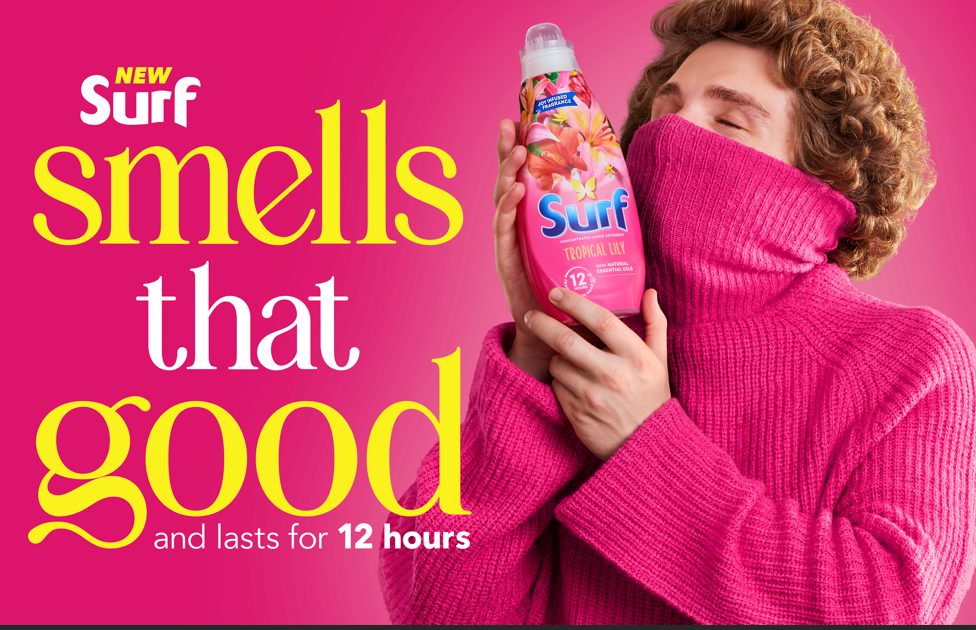 A man in a pink jumper holds up a bottle of surf and lifts up his colour as he takes in the smell of detergent. Surf gets a bold new look in MullenLowe's debut campaign for the Unilever-owned brand as it repositions itself for a more contemporary feel.